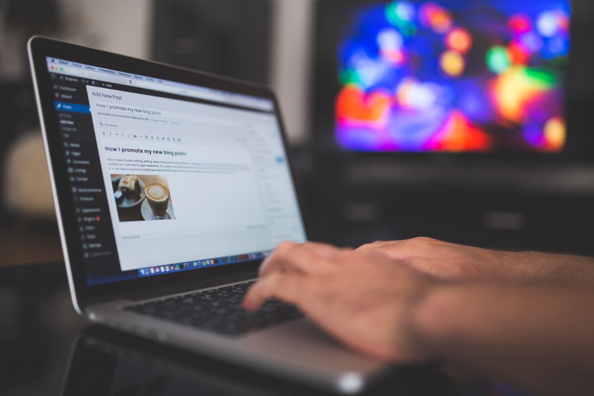 Hands typing on a laptop keyboard while editing a blog post on screen in a dimly lit room